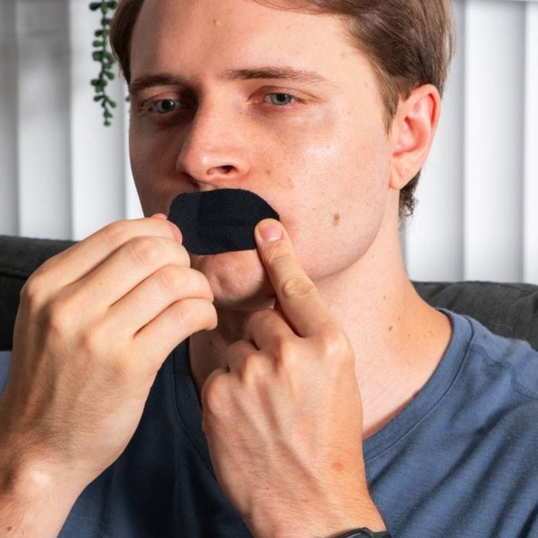 Man pressing a black Elite Sleep mouth tape strip onto his lips.